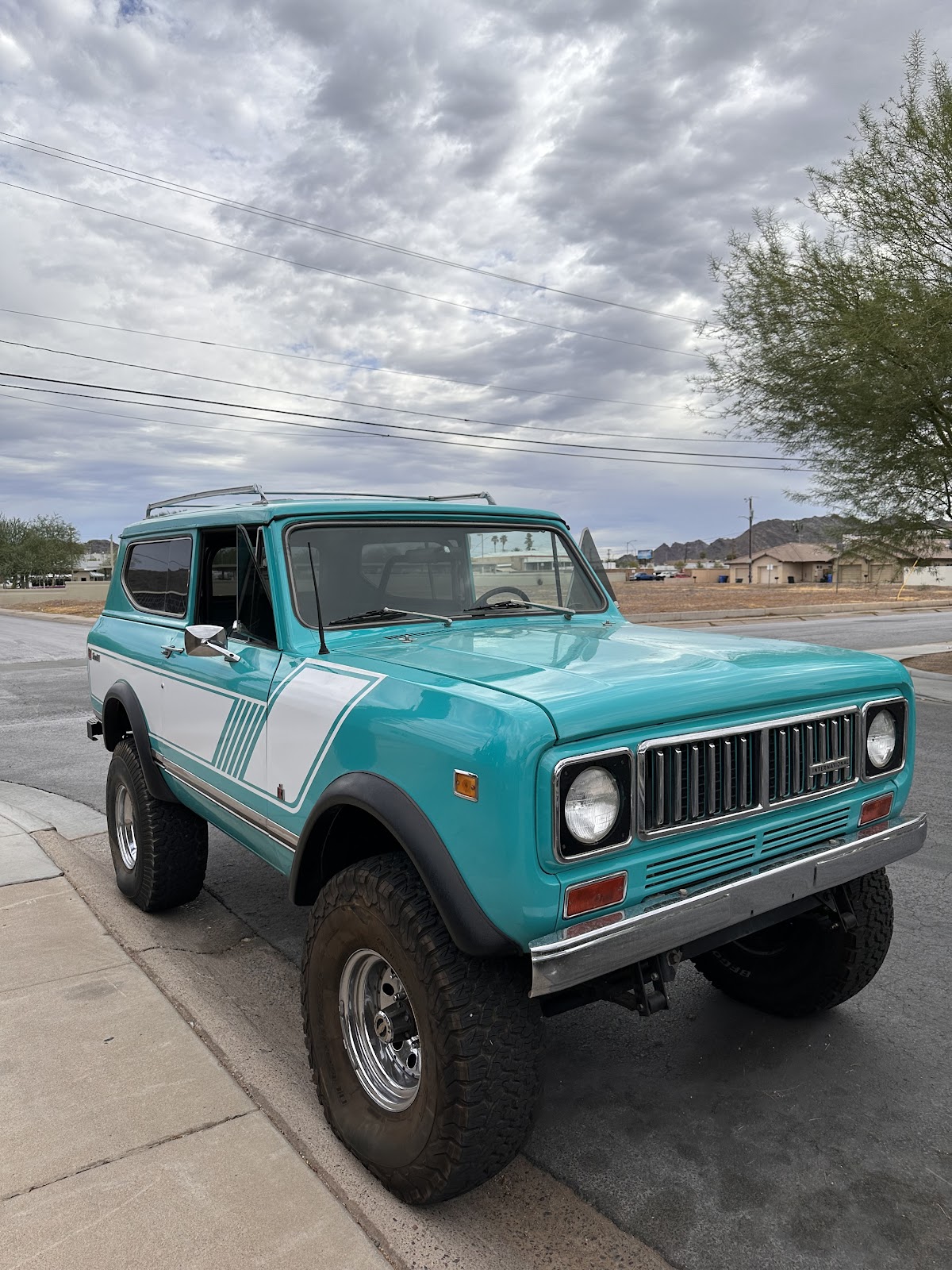 A turquoise and white International Scout truck with lifted suspension and all-terrain tires parked on a street
