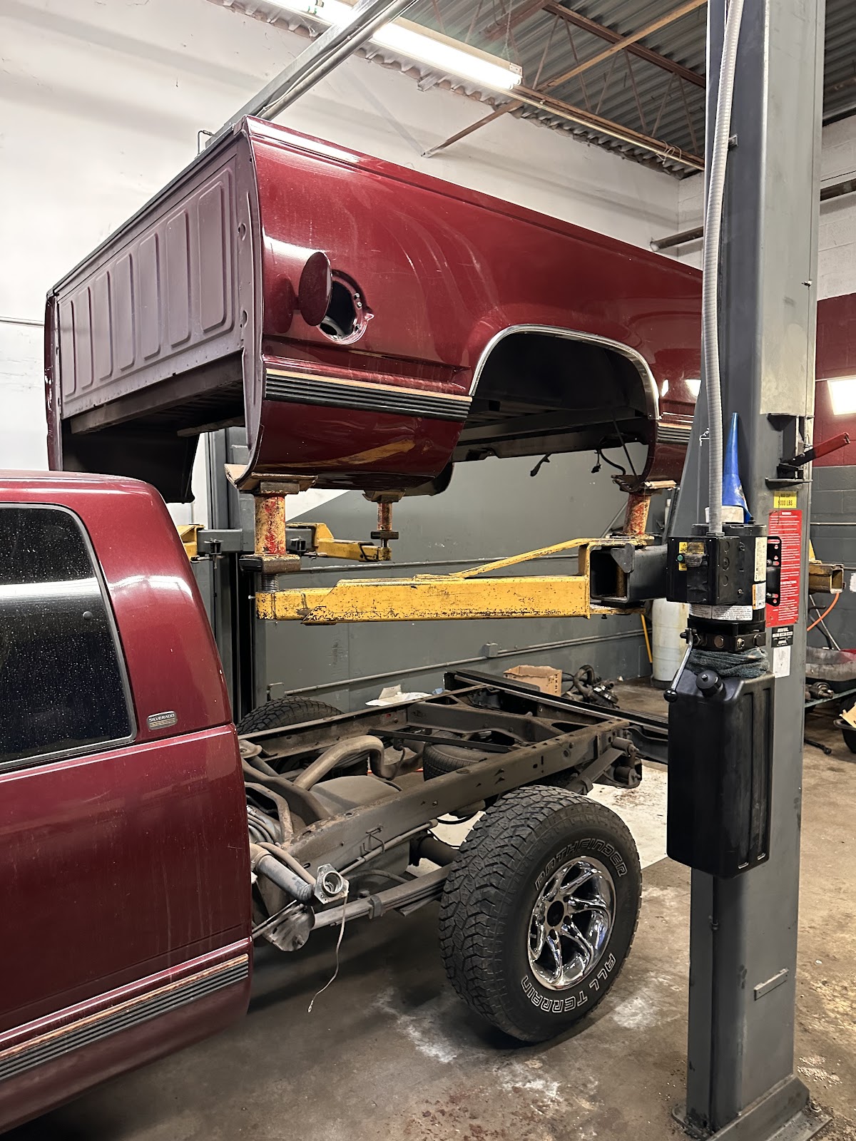 A maroon Silverado with its truck bed lifted off the frame on the two-post lift